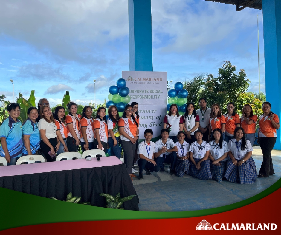 A group photo of school staff, students, and Calmar Land representatives gathered at the turnover ceremony for a newly donated waiting shed. The banner behind them highlights the company's commitment to corporate social responsibility.