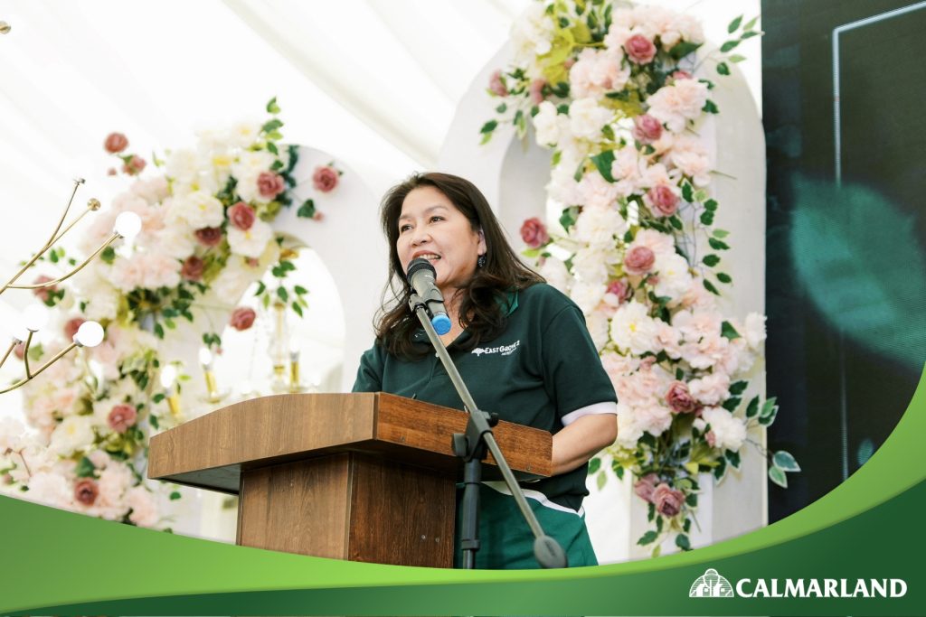 Ms. Mary Bel Calayan, President of CLDC, delivering a speech at the East Grove 2 launch event, surrounded by elegant floral decorations.